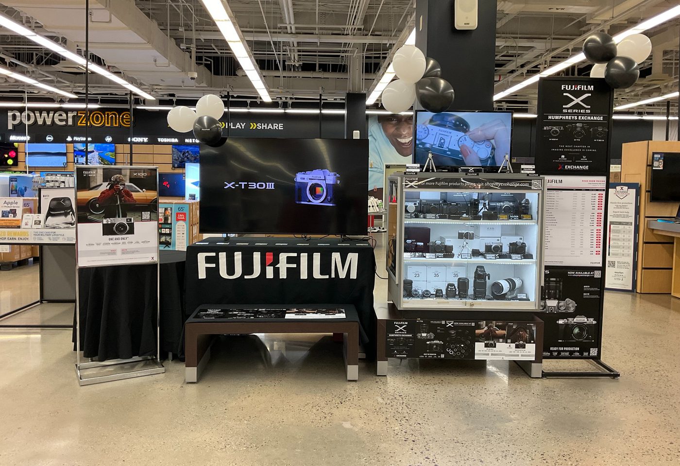 Fujifilm X Series camera display with demo screens, display case, and signage in an exchange electronics department